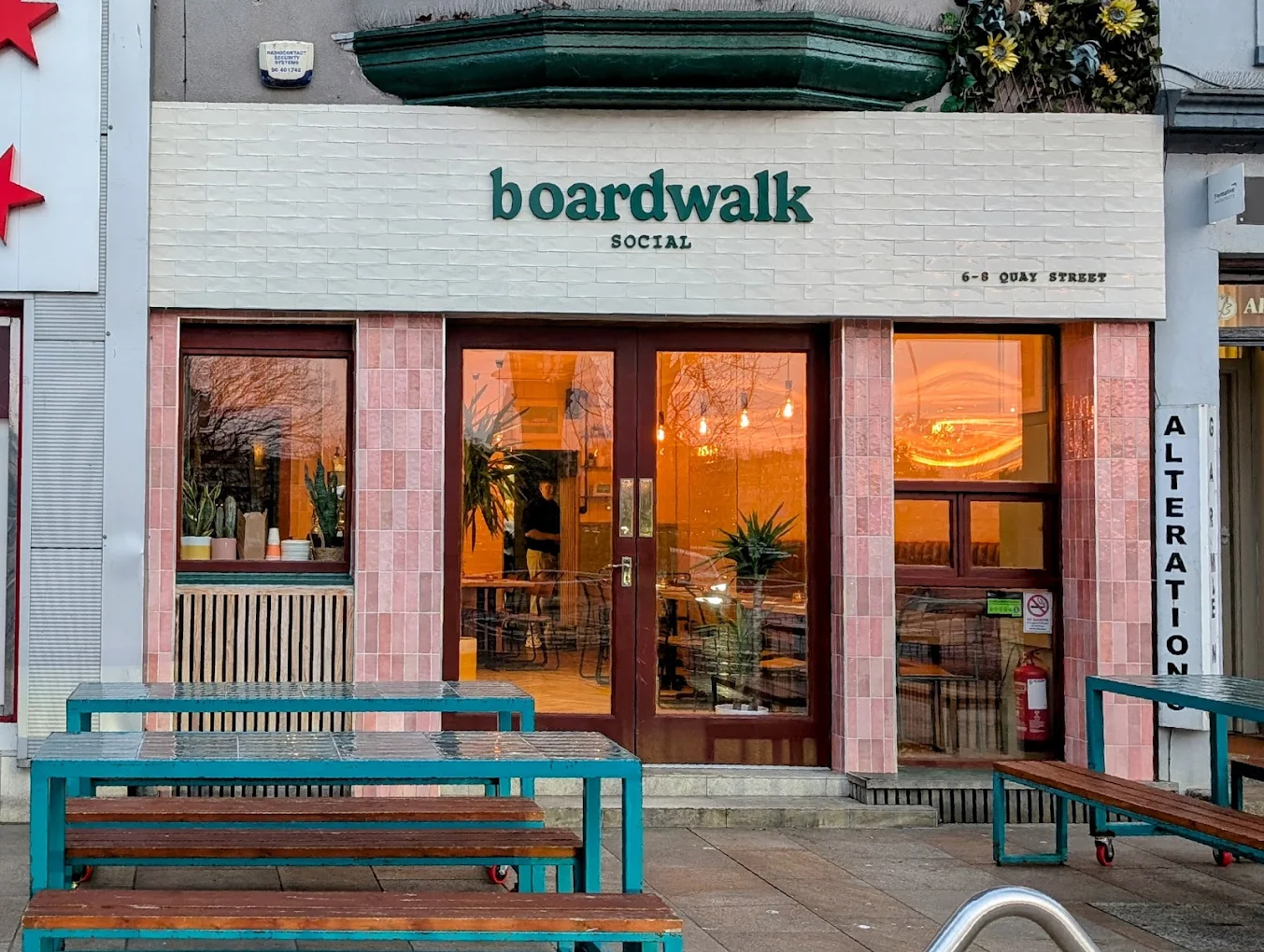 Boardwalk Social shopfront at golden hour, with pink tiles and teal picnic benches