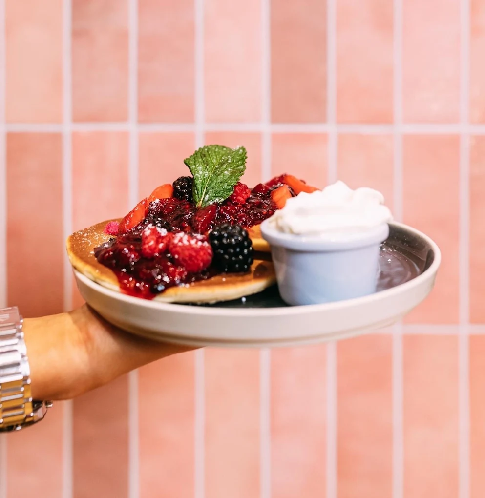 Vanilla pancakes with berry compote and whipped cream against the pink tiles